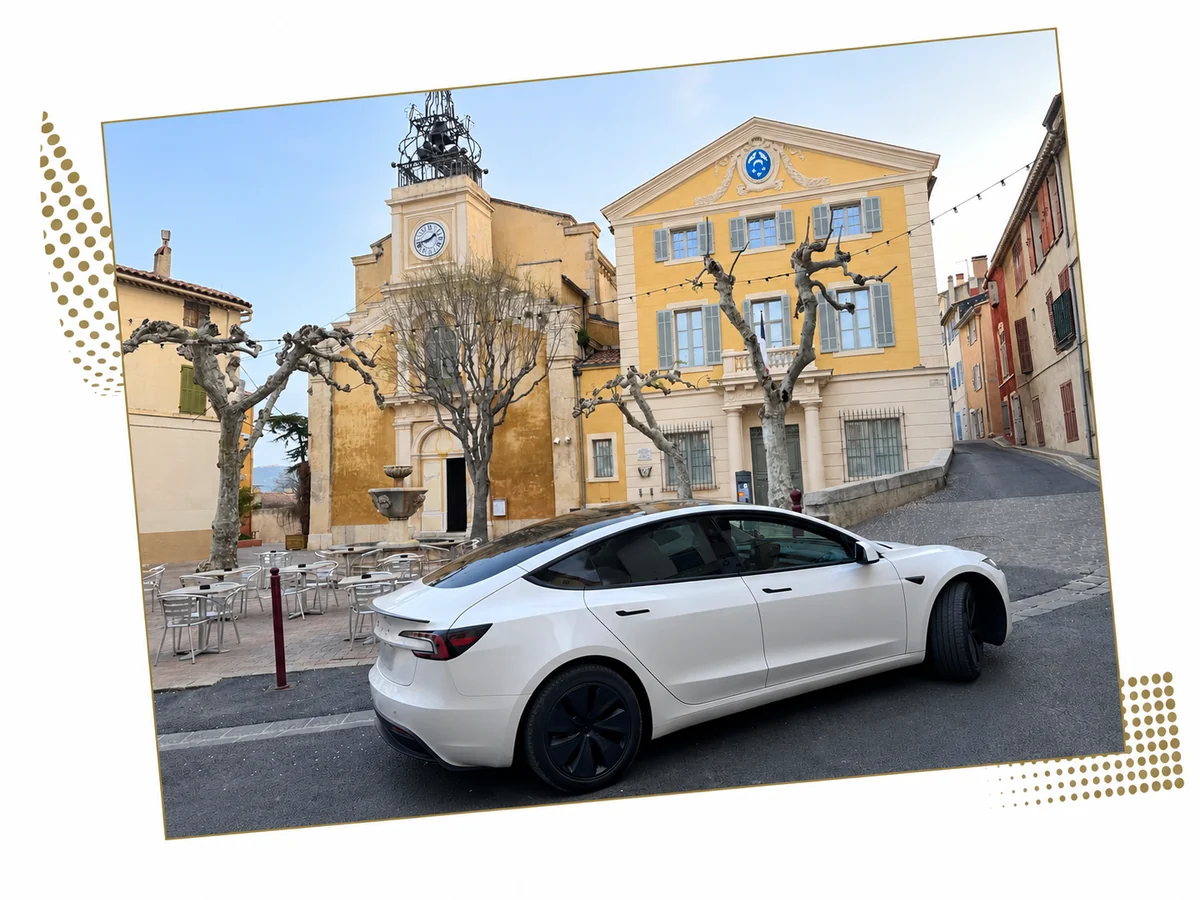 Tesla Model 3 blanche sur une place bordée de façades provençales