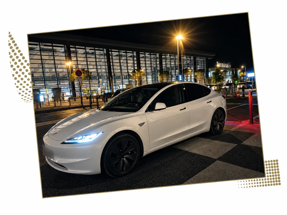 Tesla Model 3 blanche devant la façade vitrée d’un terminal de nuit