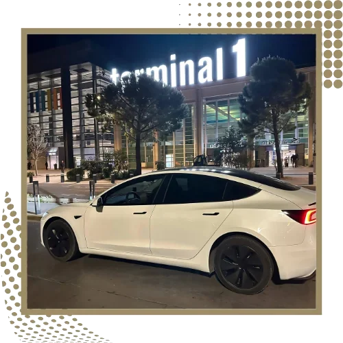 Tesla Model 3 blanche de profil devant un terminal éclairé de nuit